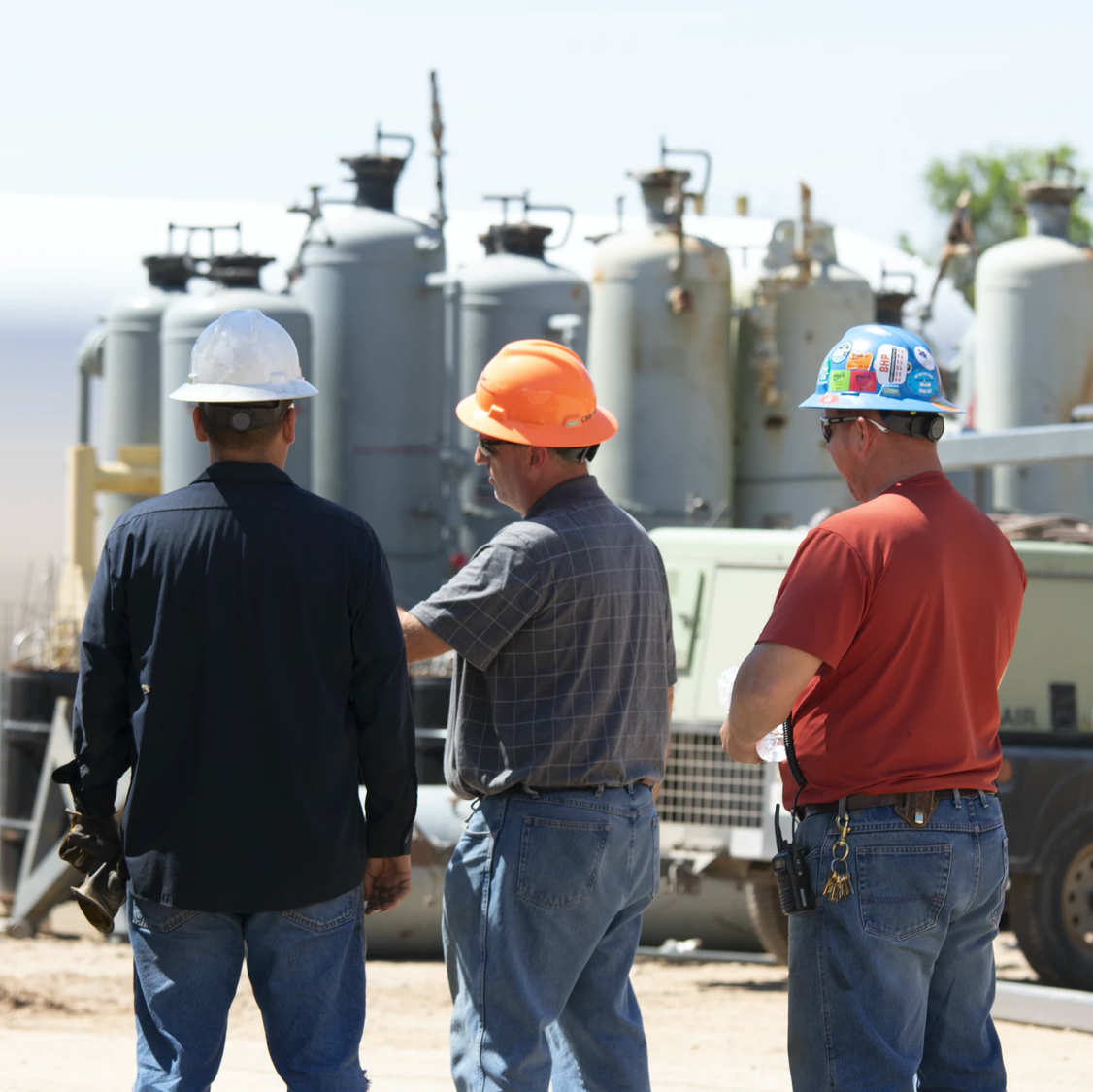 Three men in hard hats standing next to a truck.